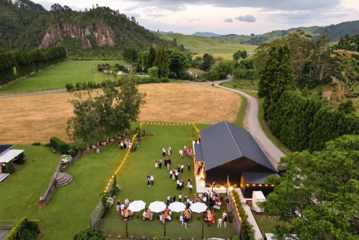 Aerial view of Stonewood Farm’s wedding barn and gardens, with guests beneath festoon lights and surrounding Coromandel countryside.